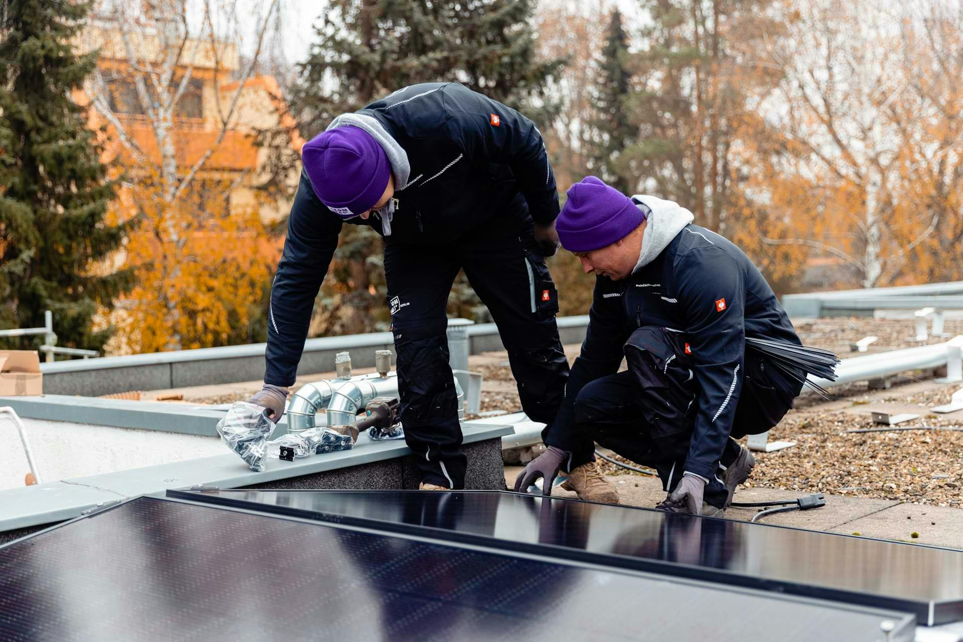Two men install a solar panel with 1KOMMA5° merchandise